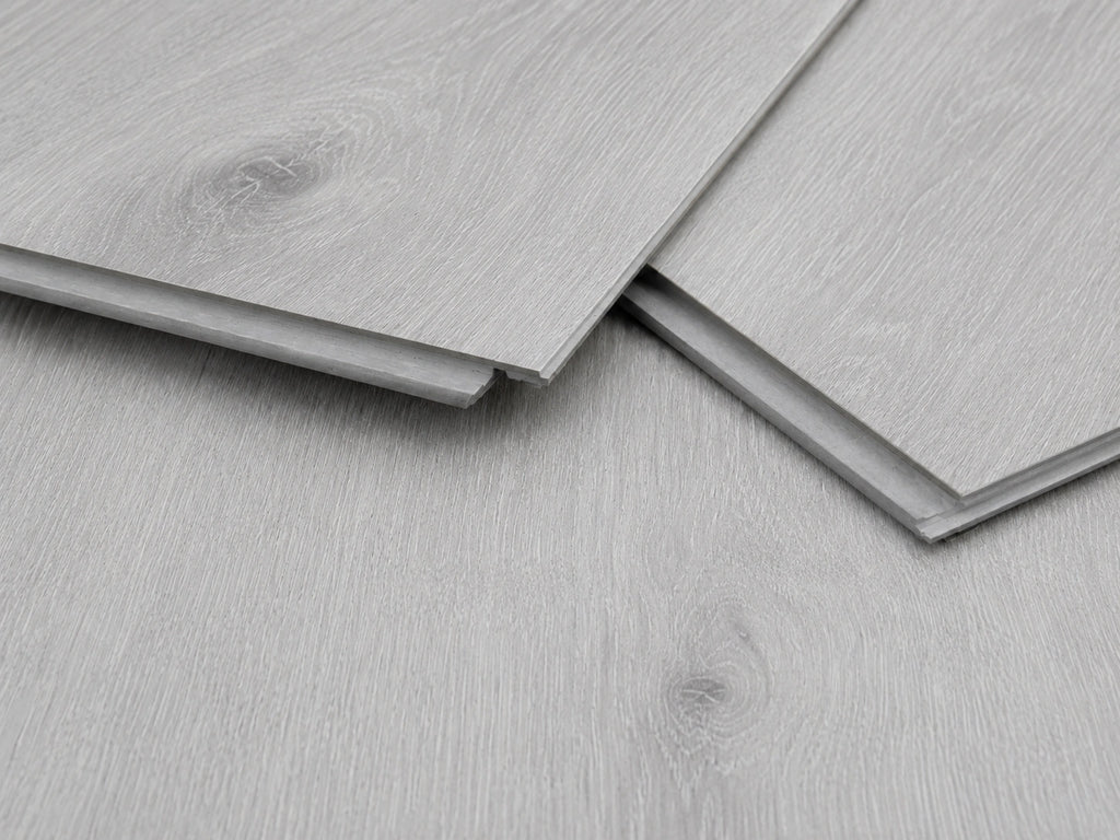 Close-up of Grey Oak SPC click-lock planks showing the rigid core profile, tongue and groove joint and brushed grey oak surface finish