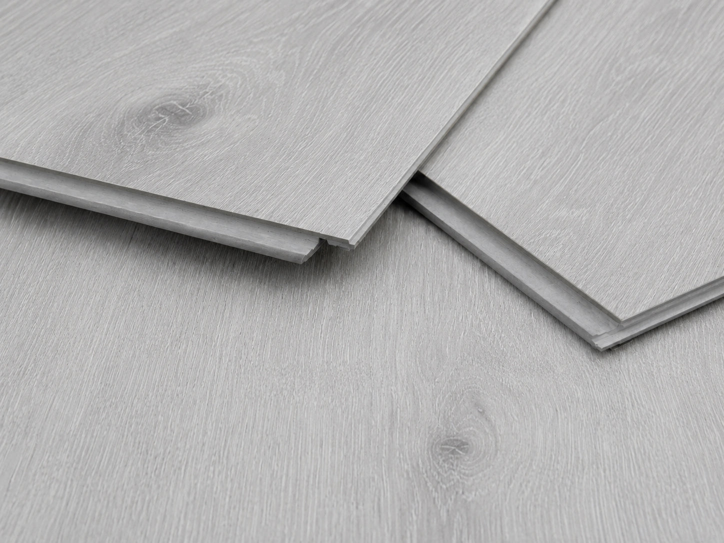 Close-up of Grey Oak SPC click-lock planks showing the rigid core profile, tongue and groove joint and brushed grey oak surface finish