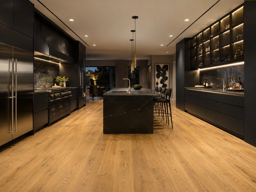 Harvest Oak SPC flooring laid in a luxury dark kitchen with black marble island, gold pendant lighting and matte black cabinetry