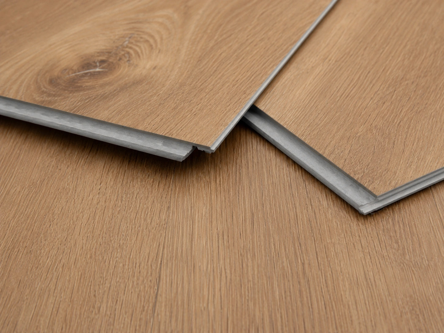 Close-up of Maple Oak SPC click-lock planks showing the rigid core profile, tongue and groove joint and warm oak surface finish
