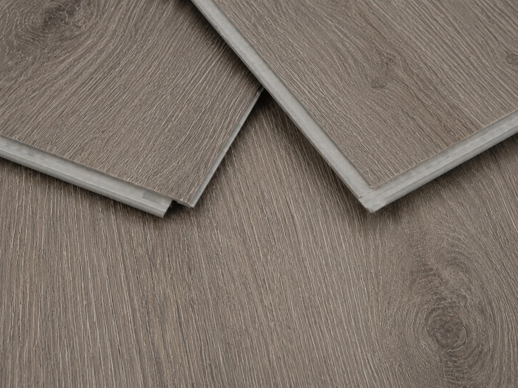 Close-up of Seasoned Oak SPC click-lock planks showing the rigid core profile, tongue and groove joint and brushed greige oak surface finish