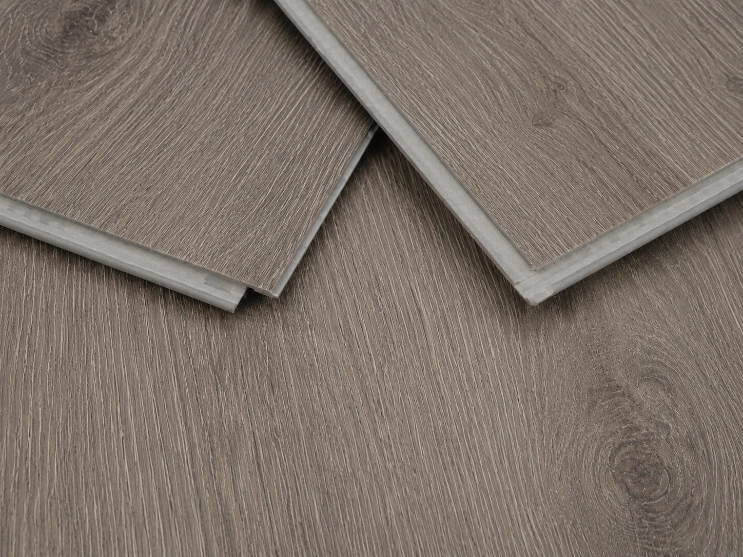 Close-up of Seasoned Oak SPC click-lock planks showing the rigid core profile, tongue and groove joint and brushed greige oak surface finish